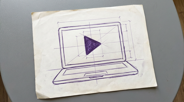 a laptop computer, open and viewed from the front, with a large, centered play button icon (a solid right-pointing triangle) displayed on its screen